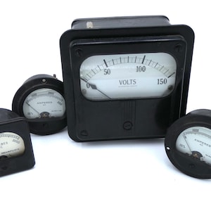 May include: A selection of antique electrical meters with black housings. The meters show readings in volts and amperes, featuring white faces and black needles. The largest meter is labelled "VOLTS", the smaller ones "AMPERES AC".