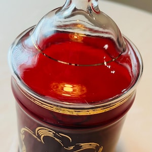 May include: A red glass jar with a gold lid and a gold inscription that reads "40th Anniversary".
