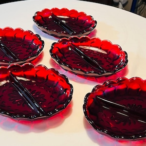 May include: Five ruby red glass serving dishes with a scalloped edge. Each dish is divided into two sections and features a floral design. The dishes are arranged on a white surface.