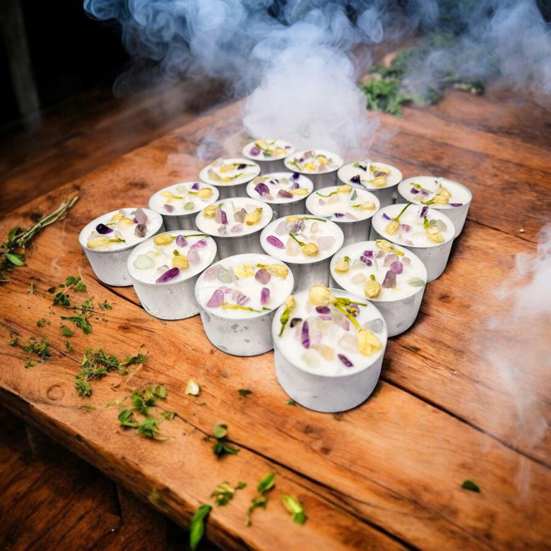 May include: A wooden table with a collection of small white candles. Each candle is topped with a mixture of purple, white, and yellow flower petals. The candles are arranged in a square shape. There is smoke rising from the candles.