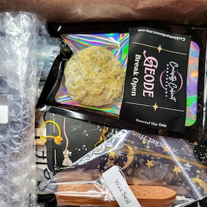 May include: A box filled with various items, including a geode, a wax seal, and a geode slice. The geode is in a clear plastic bag with a label that reads "GEODE Break Open External Use Only". The wax seal is in a clear plastic bag with a label that reads "Wax Seal". The geode slice is in a clear plastic bag with a label that reads "Geode Slice".