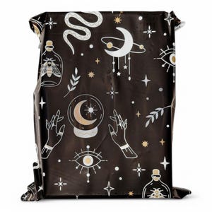 May include: Black and gold patterned fabric with a repeating design of stars, moons, eyes, snakes, hands, and bottles. The fabric has a shiny, metallic finish.