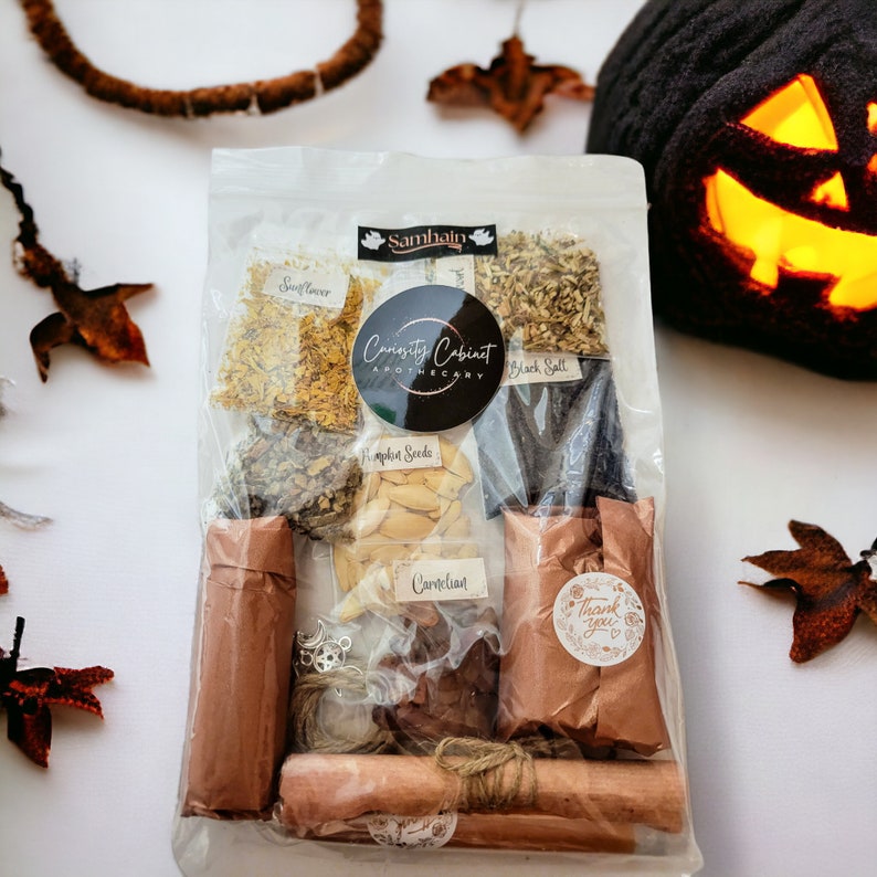 May include: A clear plastic bag filled with various herbs and spices, including sunflower, pumpkin seeds, black salt, and cardelion. The bag also contains two brown paper-wrapped bundles and a small brown paper bag with the text "Thank you" on it. The bag is labeled "Curiosity Cabinet Apothecary" and "Samhain".