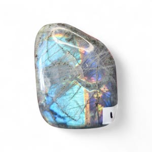 May include: A polished, oval-shaped labradorite gemstone. The stone displays a mix of gray, blue, and iridescent colors, with flashes of rainbow hues. The surface has natural cracks and variations, adding to its unique appearance. The gemstone is set against a white background.