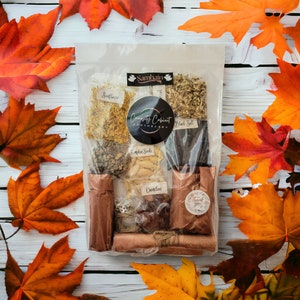 May include: A clear plastic bag filled with various ingredients for a Samhain spell kit. The bag includes sunflower petals, pumpkin seeds, black salt, and other herbs. The bag also includes a small brown paper bag with the text "Thank You" on it. The bag is labeled "Curiosity Cabinet Apothecary" and "Samhain".