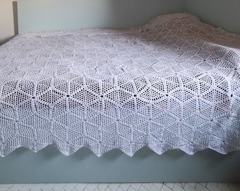 May include: White crocheted bedspread with a diamond pattern. The bedspread is made of a delicate, lacy yarn and has a scalloped edge.