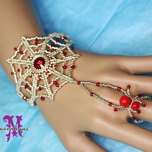 May include: A gold and red beaded bracelet with a spider web design and a red spider ring. The bracelet is on a model's hand.