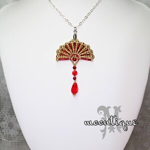 Op de afbeelding: Een gouden en rode kralen ketting met een waaier hanger aan een zilveren ketting. De waaier is gemaakt van kleine gouden en rode kralen en heeft een rode kristallen druppel.