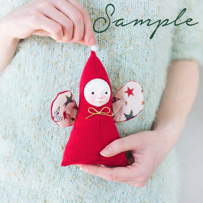 May include: A handmade red felt angel doll with a white face, gold ribbon, and wings made of patterned fabric with stars and moons.