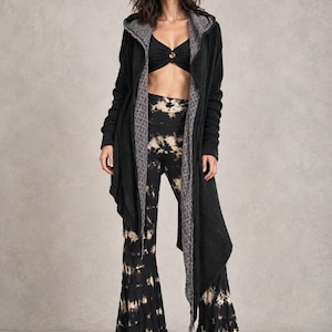 May include: A black long-sleeved hooded cardigan with a gray textured inner lining, worn over a black cropped top with a center ring detail and matching black and beige tie-dye print flared trousers with a high-waisted silhouette.