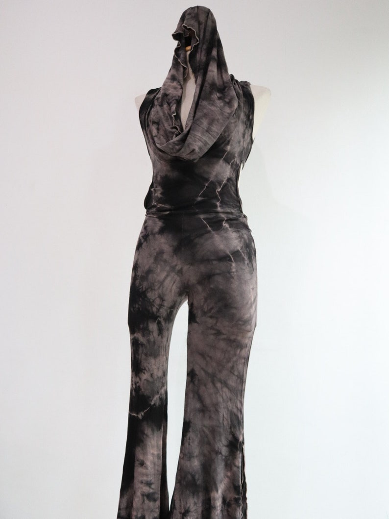 Puede incluir: Un mono de color negro y gris con estampado tie-dye, cuello de pico y piernas anchas.