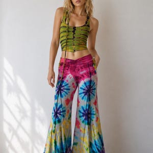 May include: A tie-dye outfit featuring a green and black striped crop top and flared pants. The pants have a vibrant tie-dye pattern with pink, blue, and yellow hues. The outfit is a bohemian style.
