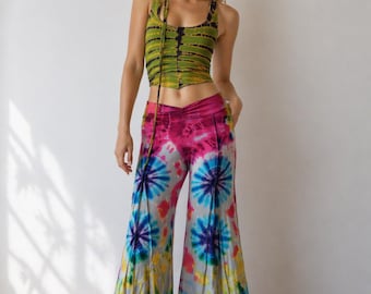May include: A tie-dye outfit featuring a green and black striped crop top and flared pants. The pants have a vibrant tie-dye pattern with pink, blue, and yellow hues. The outfit is a bohemian style.