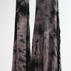 Puede incluir: Pantalones acampanados de color negro y gris con estampado tie-dye y dobladillo sin rematar.