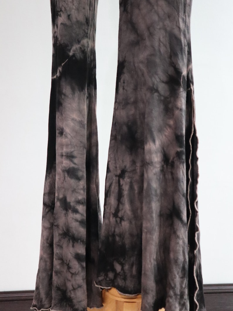 Puede incluir: Pantalones acampanados de color negro y gris con estampado tie-dye y dobladillo sin rematar.