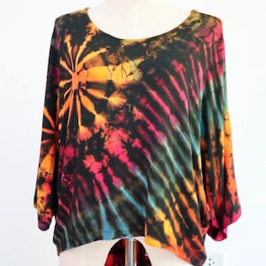 Può includere: Una maglietta tie-dye con sfondo nero e vortici colorati di arancione, giallo, rosso, rosa, blu e verde. La maglietta ha un collo rotondo e maniche 3/4.