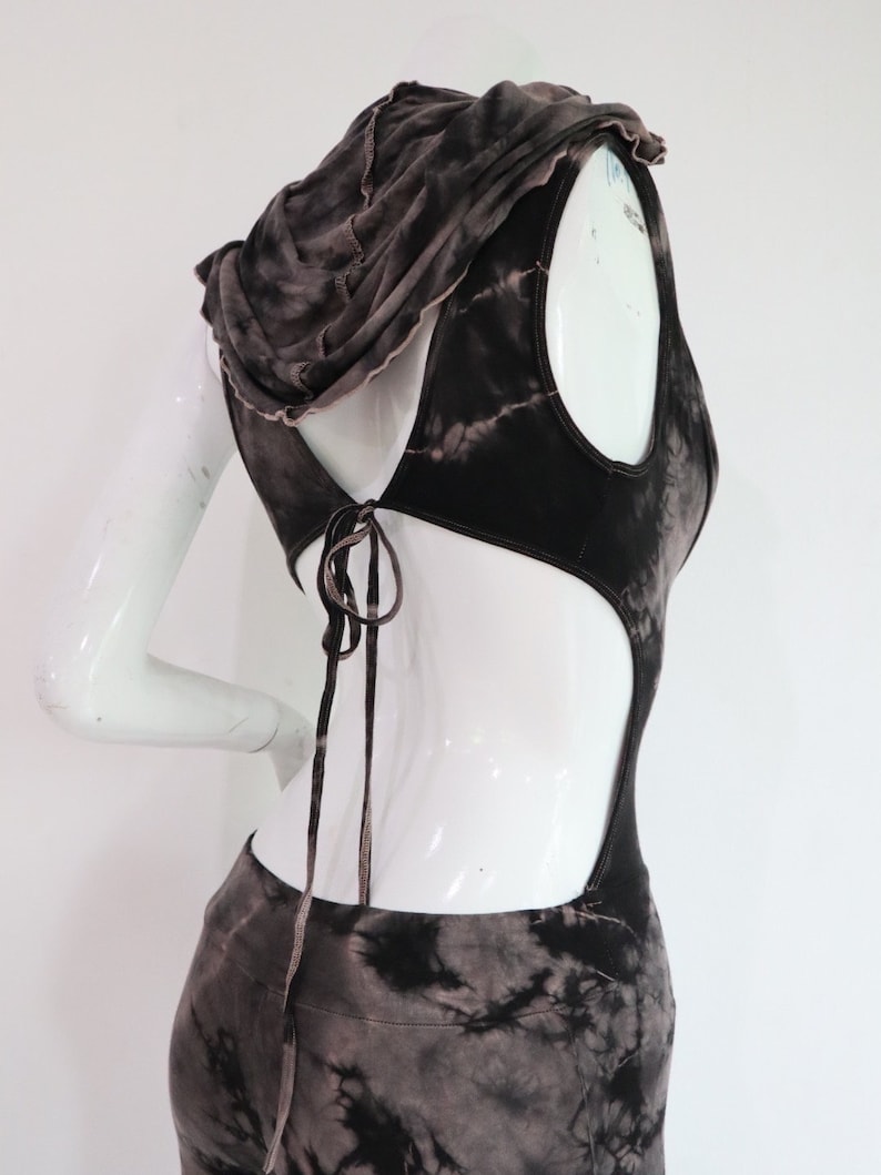 Puede incluir: Un mono con capucha de color marr&oacute;n y negro con estampado tie-dye, con la espalda recortada y un lazo en la parte posterior del cuello.