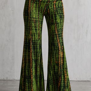 May include: High-waisted flared pants featuring a vertical tie-dye pattern in shades of forest green, black, and muted brown. The garment has a wide, fitted waistband and a long, flowing silhouette that widens significantly toward the hemline.