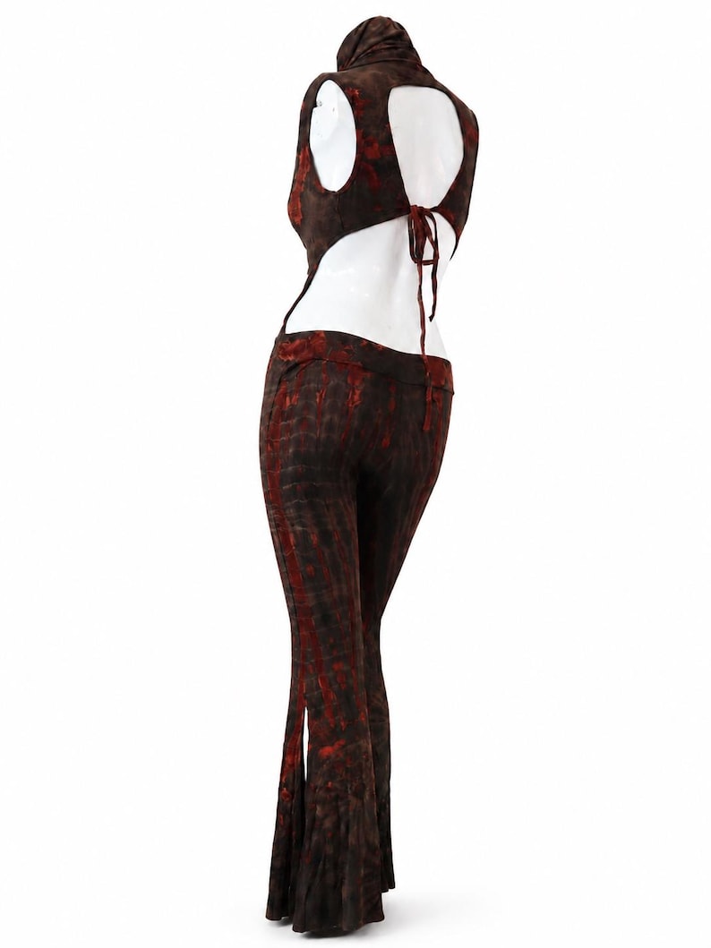 May include: A two-piece outfit featuring a sleeveless top with a high neck, an open back with tie closures, and matching flared pants. The garment is made of a dark brown fabric with a mottled, tie-dye style pattern in shades of deep red.