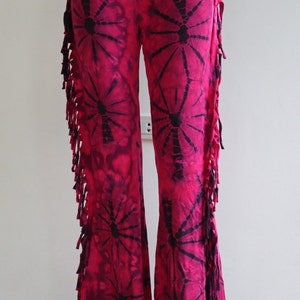 May include: Pink tie-dye bell bottom pants with black fringe and a black and pink tie-dye pattern.