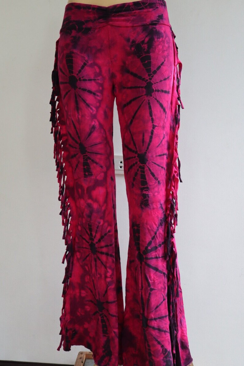 May include: Pink tie-dye bell bottom pants with black fringe and a black and pink tie-dye pattern.