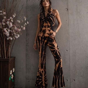 K&ouml;nnte beinhalten: Ein &auml;rmelloser Jumpsuit mit schwarz-beigem Batikmuster, Wasserfallausschnitt und ausgestellten Hosenbeinen. Das Kleidungsst&uuml;ck ist an Oberk&ouml;rper und Taille eng anliegend geschnitten und geht in weit ausgestellte Beinabschl&uuml;sse &uuml;ber.