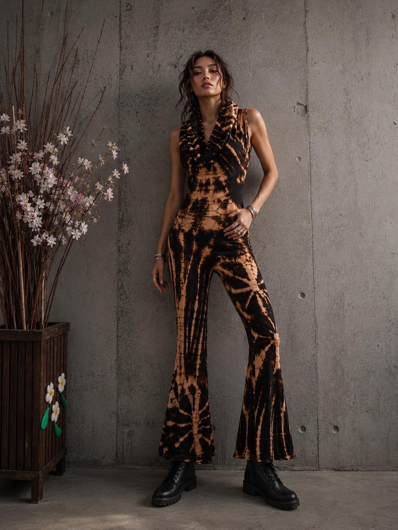 K&ouml;nnte beinhalten: Ein &auml;rmelloser Jumpsuit mit schwarz-beigem Batikmuster, Wasserfallausschnitt und ausgestellten Hosenbeinen. Das Kleidungsst&uuml;ck ist an Oberk&ouml;rper und Taille eng anliegend geschnitten und geht in weit ausgestellte Beinabschl&uuml;sse &uuml;ber.
