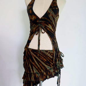 Puede incluir: Un top halter de color marrón y verde con estampado tie-dye, con un corte en la parte delantera y una falda a juego con el dobladillo con volantes. El top tiene un cierre de cordón en la cintura.