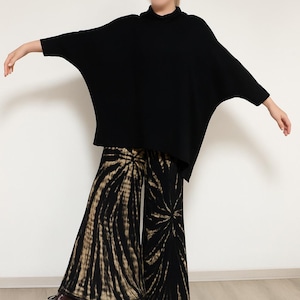 May include: A black oversized turtleneck sweater with long sleeves and a pair of wide-leg trousers with a black and tan tie-dye pattern.