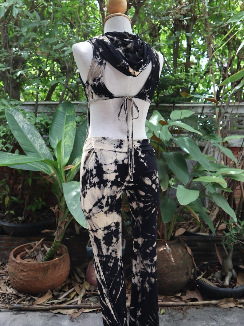 Puede incluir: Un mono de color negro y blanco tie-dye con una parte superior sin mangas y una capucha. La parte superior tiene un lazo en la parte posterior.