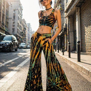 Könnte beinhalten: Ein zweiteiliges Outfit mit Batikmuster, bestehend aus einem Crop-Top und einer Schlaghose. Das Top hat eine Schnürung vorne und die Hose hat Taschen. Das Farbschema umfasst Schwarz, Orange und Türkis. Das Outfit wird in einer urbanen Umgebung getragen.