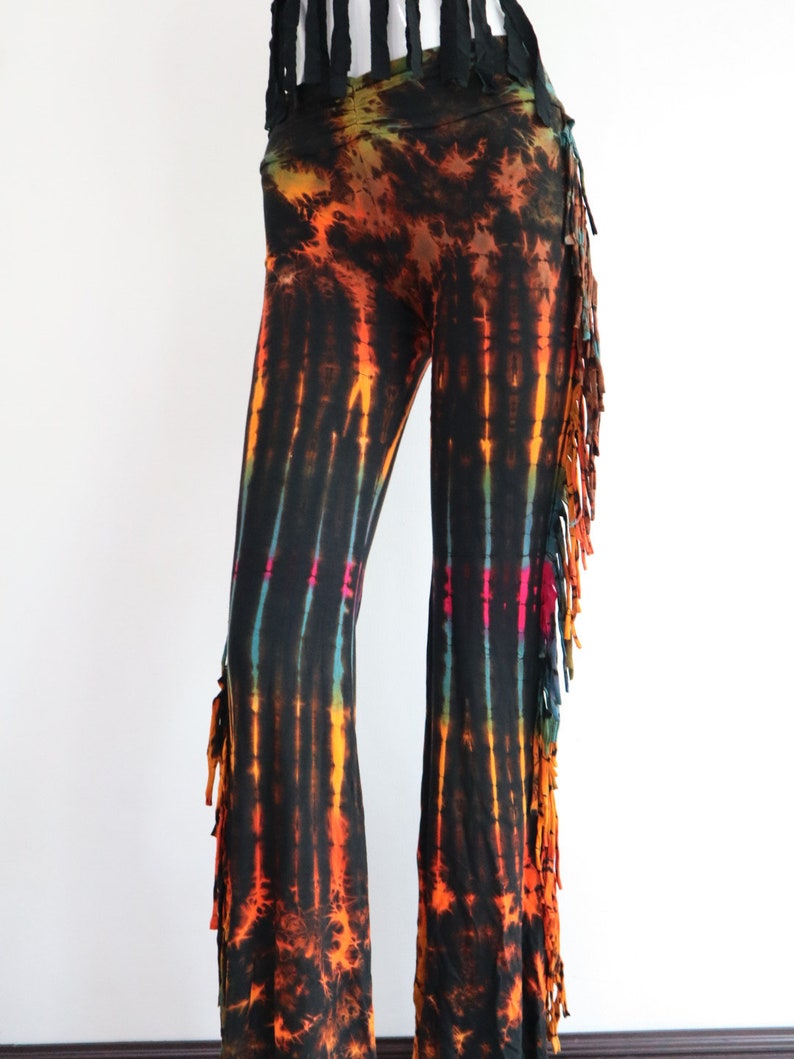May include: Black tie-dye pants with orange, yellow, and blue accents. The pants have a fringe detail on the sides.
