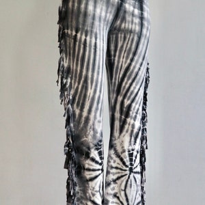 May include: Black and white tie-dye pants with fringe detail on the sides. The pants have a wide leg silhouette.