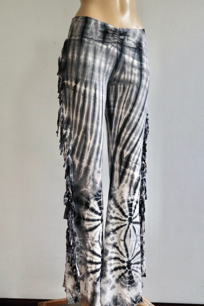 May include: Black and white tie-dye pants with fringe detail on the sides. The pants have a wide leg silhouette.