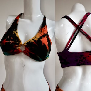 May include: A black, orange, and purple tie-dye bikini top with a criss-cross back strap design. The top has a ring detail in the front.