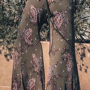 Puede incluir: Un pantalón de pierna ancha con estampado paisley en tonos verdes, rosas y negros. El pantalón tiene un lazo en la cintura y un corte holgado y fluido.