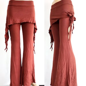 Può includere: Pantaloni svasati color ruggine con gonna asimmetrica attaccata. La gonna ha un bordo a balze e scende sui lati. I pantaloni hanno una vita alta e un design a gamba svasata. La gonna è legata su un lato.