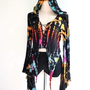 Może przedstawiać: Czarny top z kapturem w stylu tie-dye z długimi rękawami i sznurowaniem z przodu. Rękawy mają kształt dzwonu, a top jest krótki. Wzór tie-dye zawiera odcienie różowego, niebieskiego, pomarańczowego i żółtego.