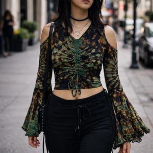 May include: A woman in a tie-dye print top with cold shoulder cutouts and bell sleeves, paired with black trousers. She wears sunglasses and a choker necklace. The background is a city street.