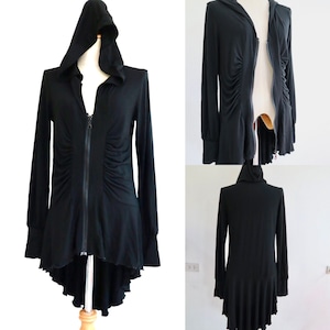 Może przedstawiać: Czarny, długorękawny top z kapturem i zamkiem błyskawicznym, z asymetrycznym dołem. Top ma falbankę na dole i marszczony detal z przodu.