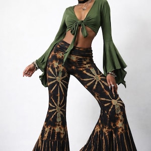 Puede incluir: Un top corto verde anudado con mangas acampanadas largas combinado con pantalones acampanados teñidos con tinte. Los pantalones presentan un patrón marrón y negro. El modelo lleva botas marrones.