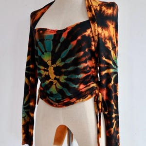 Könnte beinhalten: Ein langärmliges Batik-Oberteil mit schwarzem Hintergrund und orangefarbenen, gelben, grünen und blauen Batik-Mustern. Das Oberteil hat einen U-Boot-Ausschnitt und ist mit einem Band in der Taille gebunden.