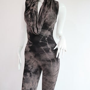 Puede incluir: Un mono de color negro y gris con estampado tie-dye, cuello de pico y sin mangas.