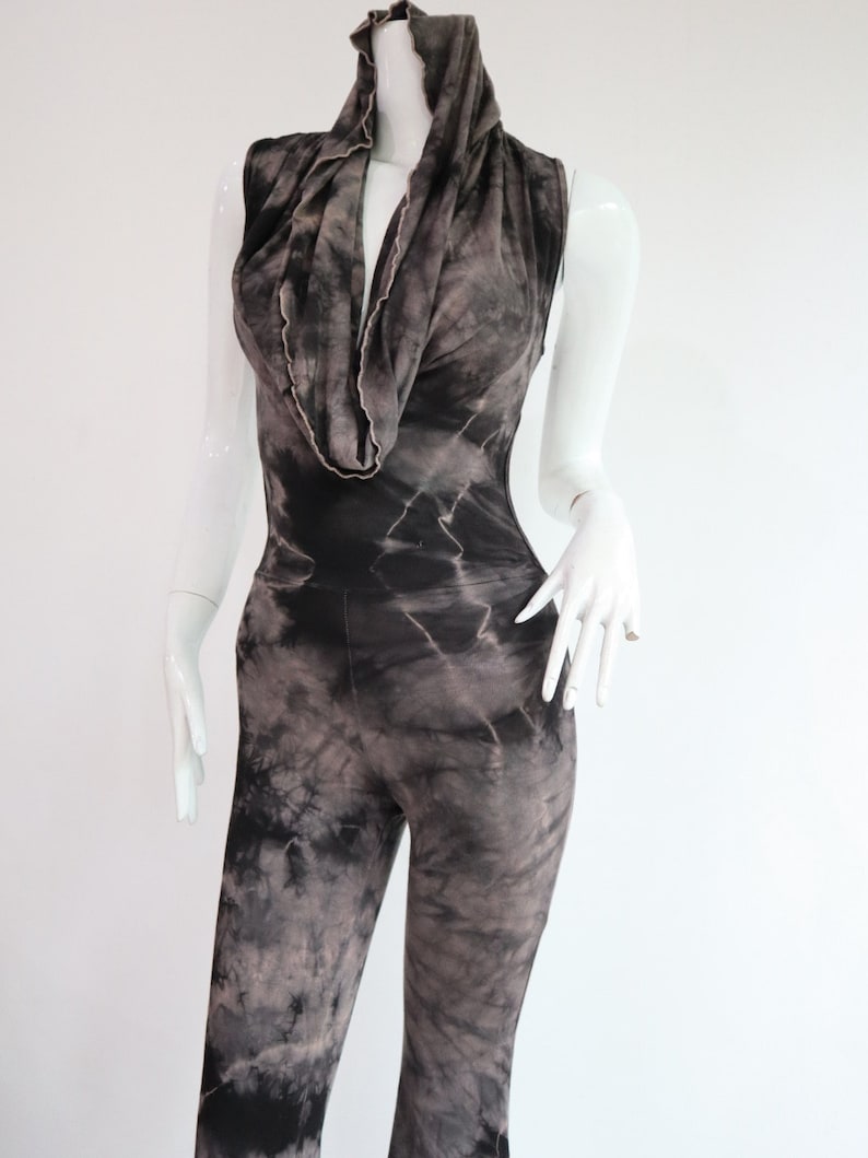 Puede incluir: Un mono de color negro y gris con estampado tie-dye, cuello de pico y sin mangas.