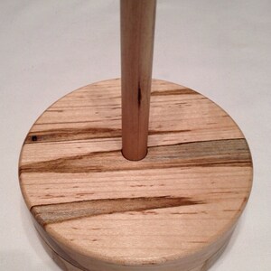 May include: A wooden yarn bowl with a natural wood finish and a round base. The bowl has a center hole for a spindle.