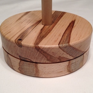May include: A wooden yarn bowl with a natural wood finish and a unique grain pattern. The bowl has a round base and a center post for holding yarn.