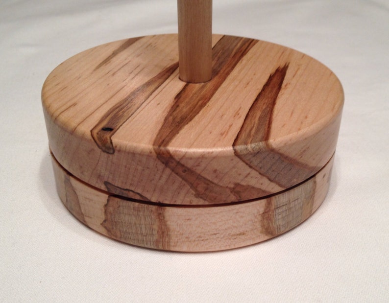 May include: A wooden yarn bowl with a natural wood finish and a unique grain pattern. The bowl has a round base and a center post for holding yarn.