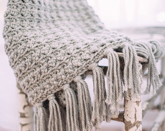 May include: A gray crocheted throw blanket with fringe hanging over a white painted chair with a distressed finish.