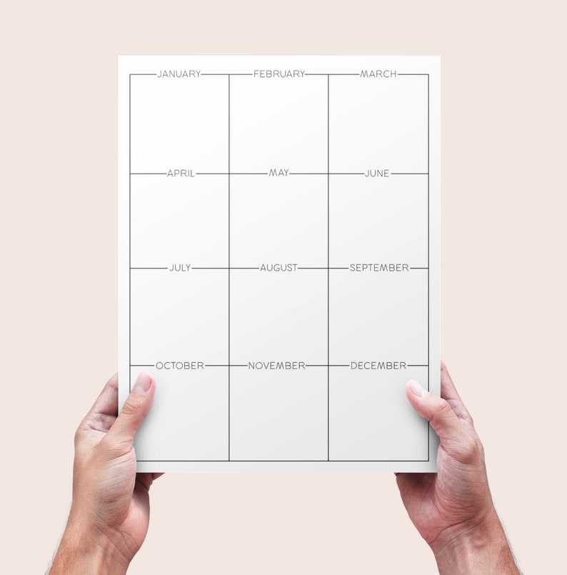 May include: A white yearly planner with a grid layout, held by two hands. The planner is divided into twelve sections, each labelled with a month from January to December. The design is minimalist with black lines and text.