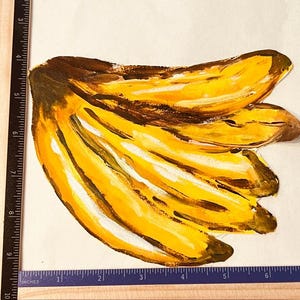 Puede incluir: Una ilustración pintada a mano de un racimo de plátanos en tonos amarillos y marrones. La obra está colocada junto a una regla, mostrando que el racimo mide aproximadamente 16,5 cm de ancho y 19 cm de alto sobre el papel.